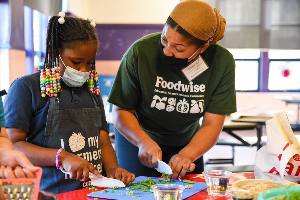 A child and Foodwise staff member chopping vegetables together